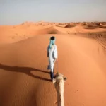 Person in weißer Kleidung geht allein durch die orangefarbenen Sanddünen der Sahara