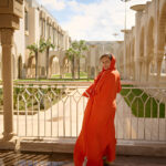 Frau in rotem Kleid posiert auf einem weißen Balkon vor einer prunkvollen arabischen Architektur