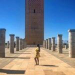 Person steht zwischen antiken Säulen vor dem Hassan-Turm in Rabat bei blauem Himmel