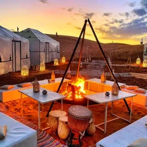 Gemütliches Wüstencamp bei Sonnenuntergang mit Zelten, Lagerfeuer, Trommeln und traditionellen Sitzbereichen