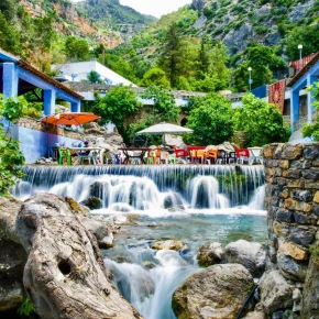Terrasse mit bunten Stühlen an einem Wasserfall in den Bergen von Akchour bei Chefchaouen, umgeben von grüner Natur