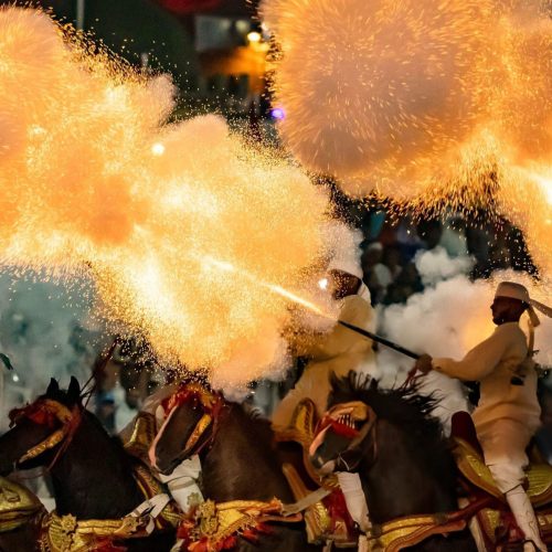 Traditionelle marokkanische Fantasia-Vorführung mit Reitern in weißer Kleidung, die synchron Gewehre abfeuern
