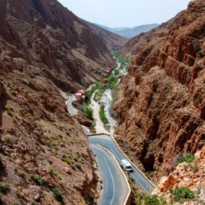 Serpentinenstraße durch die enge Felsenschlucht des Dades-Tals mit Fluss und Fahrzeugen