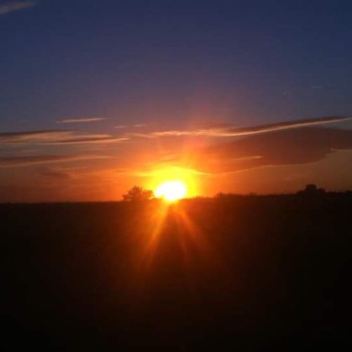 Sonnenaufgang über einer flachen Landschaft mit leuchtend orangenem Himmel und dunklem Horizont