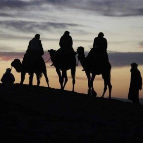 Silhouetten von Menschen auf Kamelen bei Sonnenuntergang auf einer Sanddüne in der Sahara