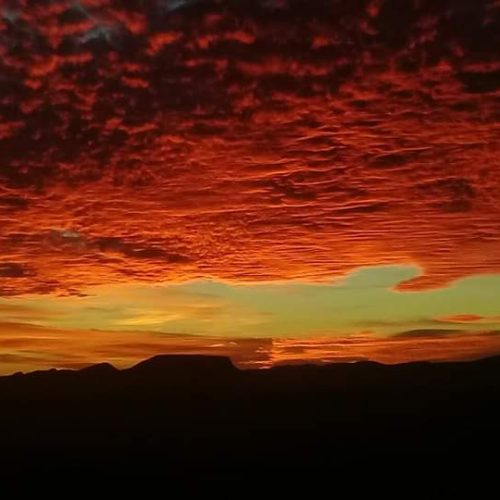 Dramatischer Sonnenuntergang über einer Bergsilhouette mit leuchtend rotem und orangefarbenem Wolkenhimmel