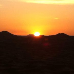 Sonnenuntergang über den Dünen der Sahara mit leuchtend orangefarbenem Himmel