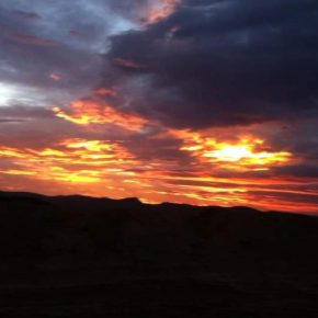Dramatischer Sonnenuntergang über der Wüste mit dunklen Wolken und orange leuchtendem Himmel