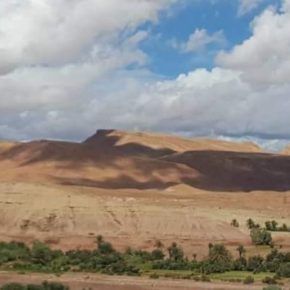 Landschaft mit sanften Hügeln, Wüstenvegetation und dramatischem Wolkenhimmel im Süden Marokkos