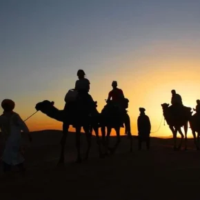Kamelkarawane in der Wüste bei Sonnenuntergang mit Menschen im Gegenlicht