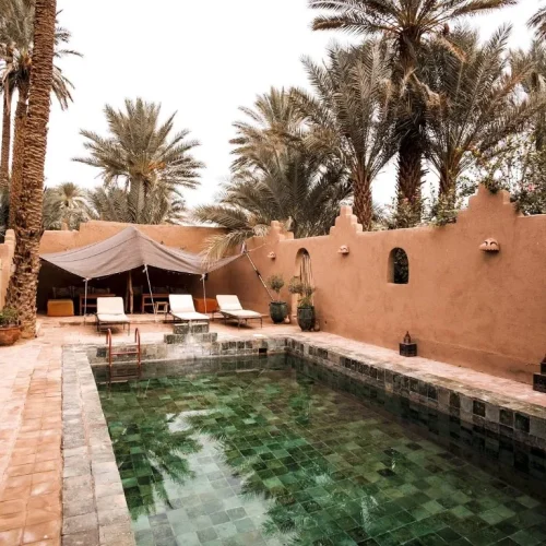 Ruhiger Innenhof mit Pool, Sonnenliegen und Palmen in traditioneller Lehmmauer-Architektur