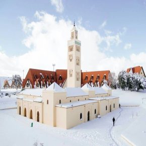 Moschee mit Minarett im Zentrum von Ifrane, Marokko, umgeben von schneebedeckten Gebäuden und blauem Himmel