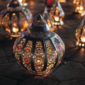 Traditionelle marokkanische Laternen aus Metall mit buntem Glas, leuchtend bei Nacht auf einem Steinboden arrangiert